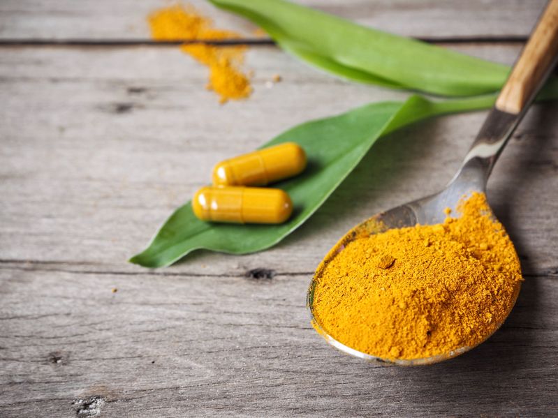 Natural turmeric and ginger root supplement capsules on a wooden surface